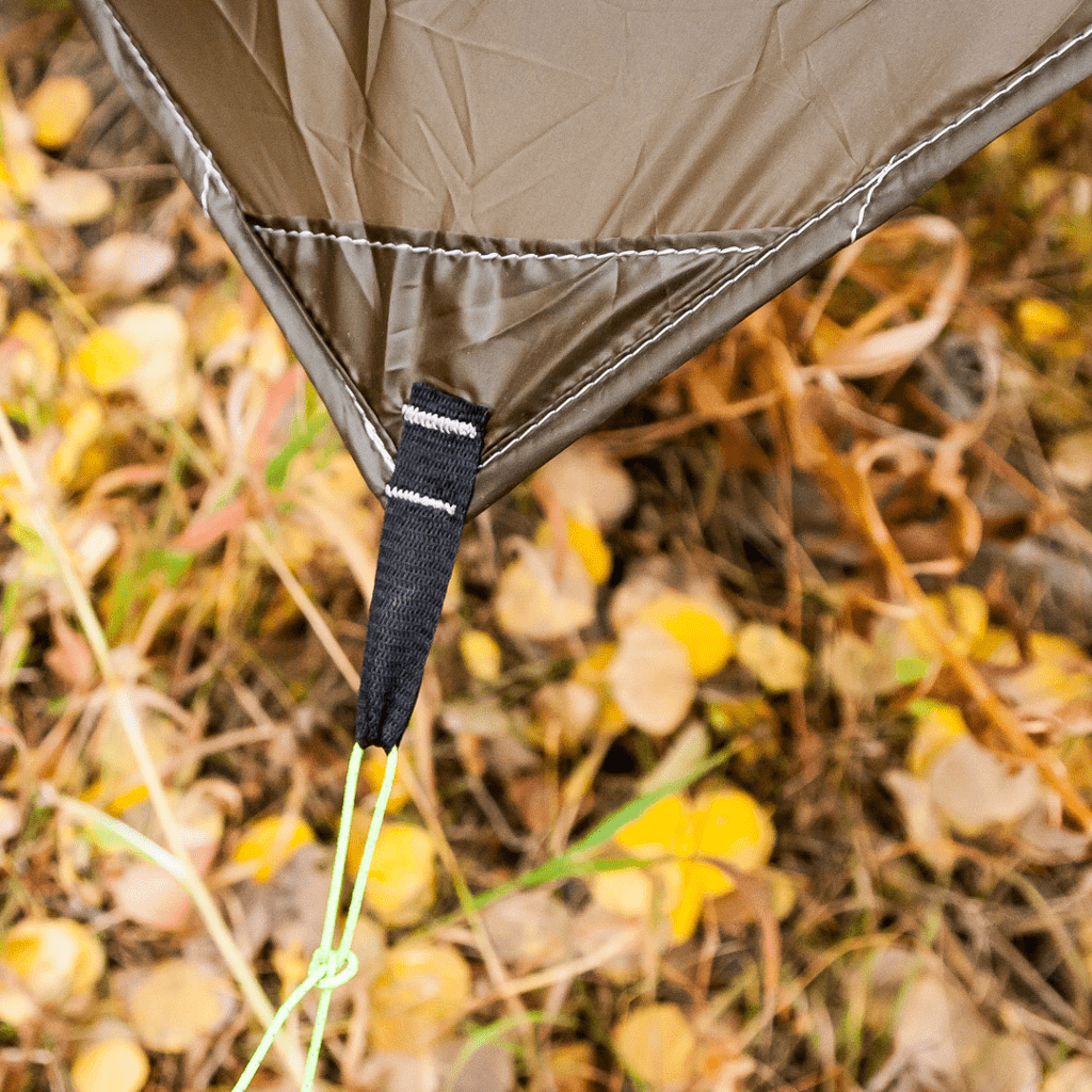 A close-up of a gray Heron Rain Tarp tail and handle on a ground covered with yellow autumn leaves, crafted from ultralight Silpoly by Hummingbird Hammocks.
