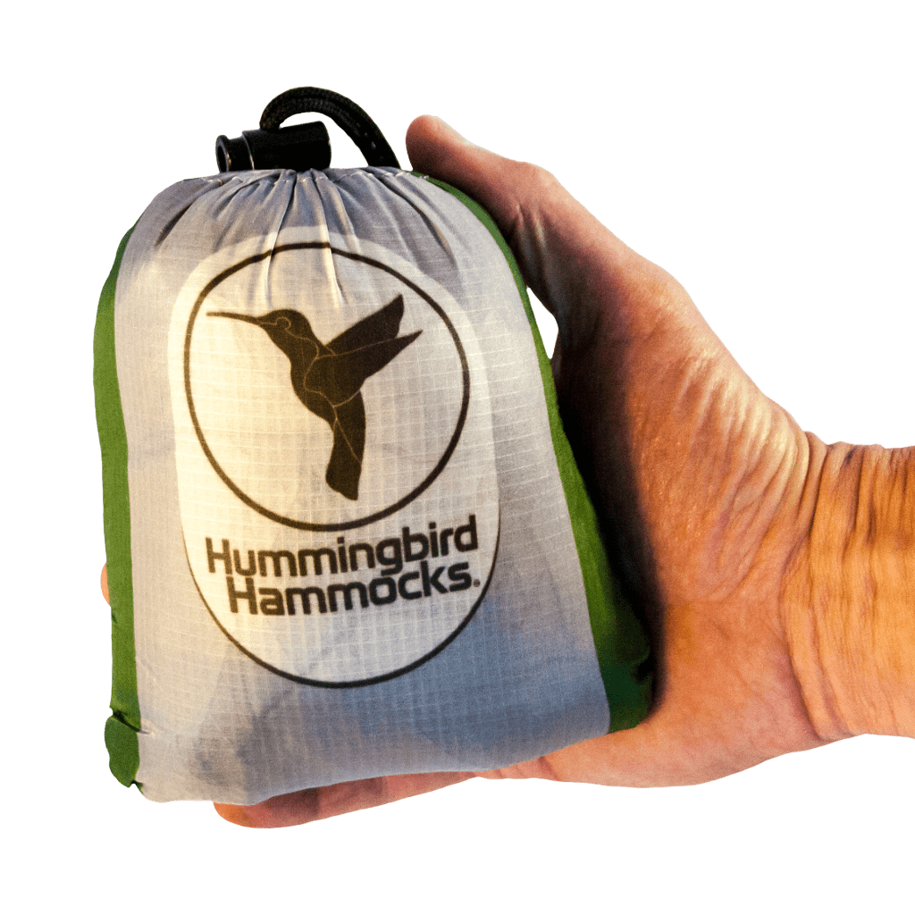 A hand holding a small, gray drawstring pouch branded with the "Hummingbird Hammocks" logo, featuring an ultralight Double Hammock design.