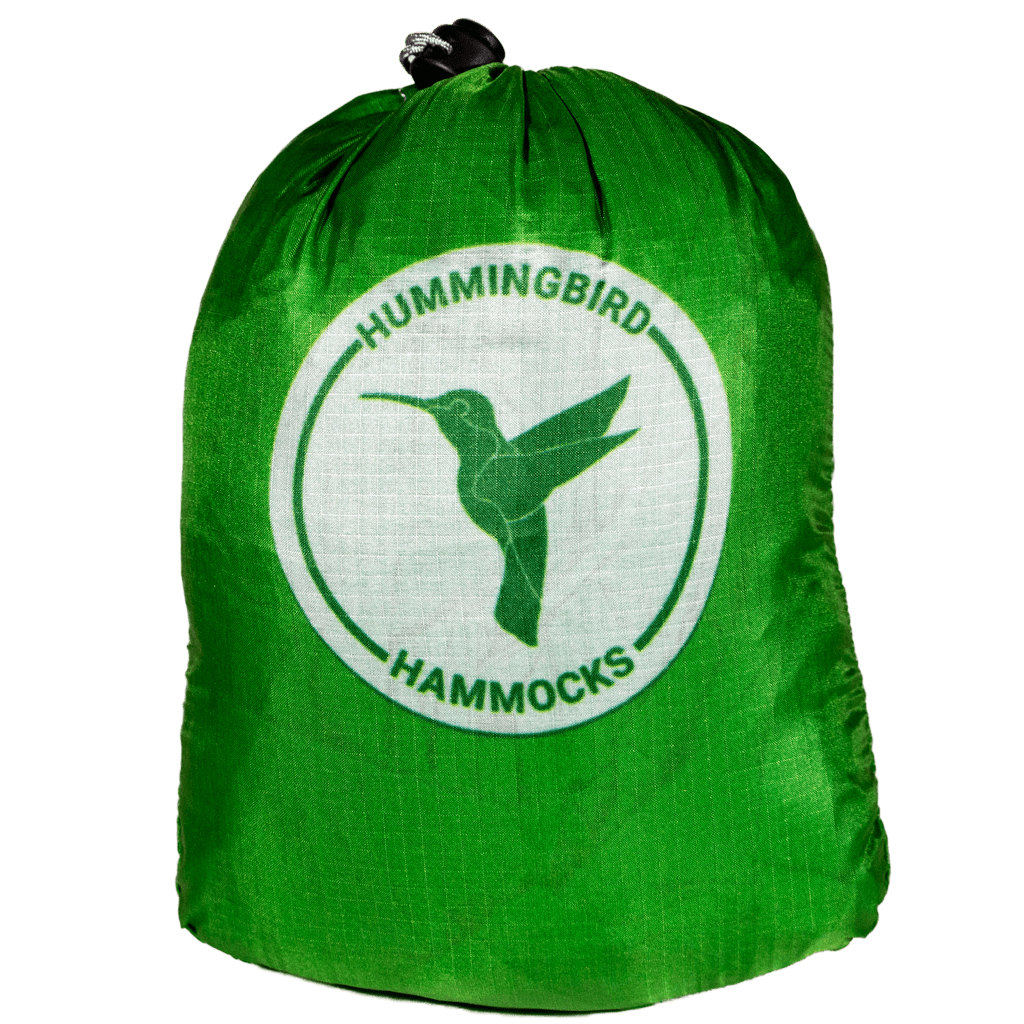 A green stuff sack with the white logo of "Hummingbird Hammocks" featuring a hummingbird silhouette, designed by an FAA Certified Parachute Rigger to hold the Long Hammock.