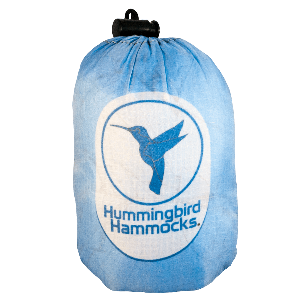 A blue compression sack with the Hummingbird Hammocks logo featuring a silhouette of a hummingbird in flight, utilizing parachute technology for the Single+ Hammock.