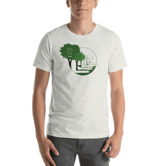 Young man in a Hummingbird Hammocks Two Trees T-Shirt with a green graphic design featuring a tree and text about global reforestation, standing against a green background.