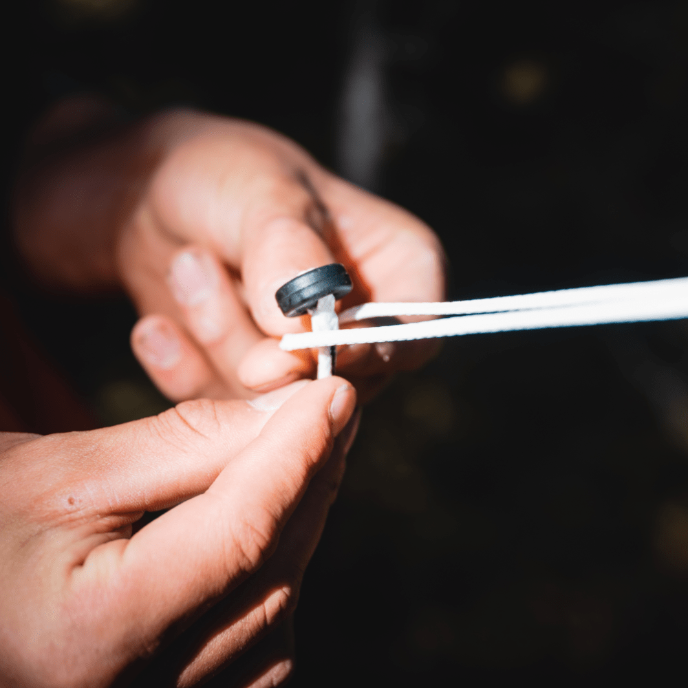 Close-up of hands sharpening a white pencil with a small black sharpener, featuring Spectra material, focused against a blurred background by Hummingbird Hammocks.