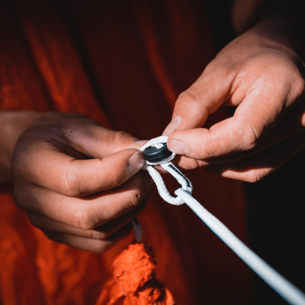 Close-up of hands threading a needle through a Replacement Button Link Set on orange Spectra fabric by Hummingbird Hammocks.