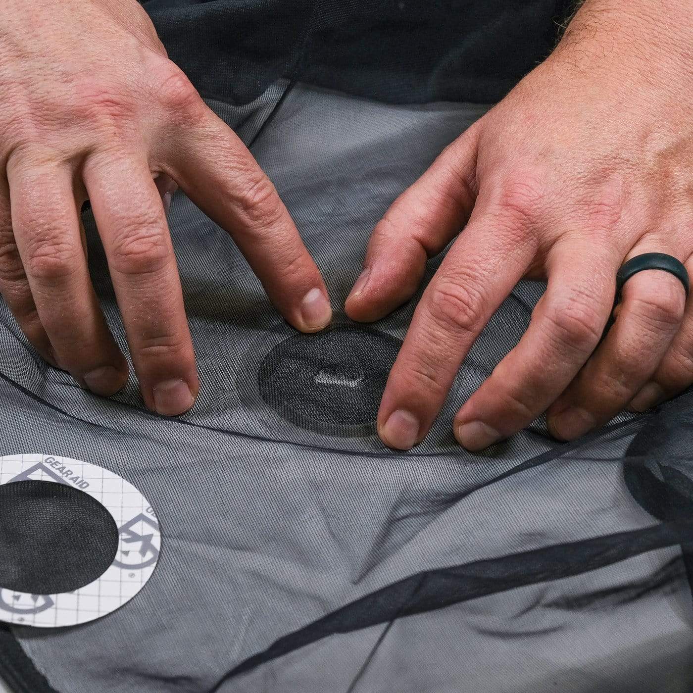 Close-up of a person's hands patching a hole in gray fabric with a Hummingbird Hammocks Tenacious Tape Mesh Patch.