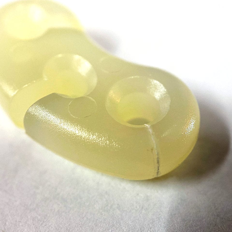 Close-up of a translucent yellow silicone Glow Friction Adjusters - Bargain Bin with circular textures, visible seam, and made by injection molding by Hummingbird Hammocks.