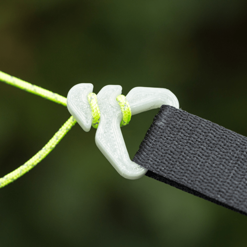 Close-up of a transparent plastic cord lock on a neon green drawstring and black fabric tab, set against a blurred green background, ideal for securing a Pelican Rain Tarp from Hummingbird Hammocks.