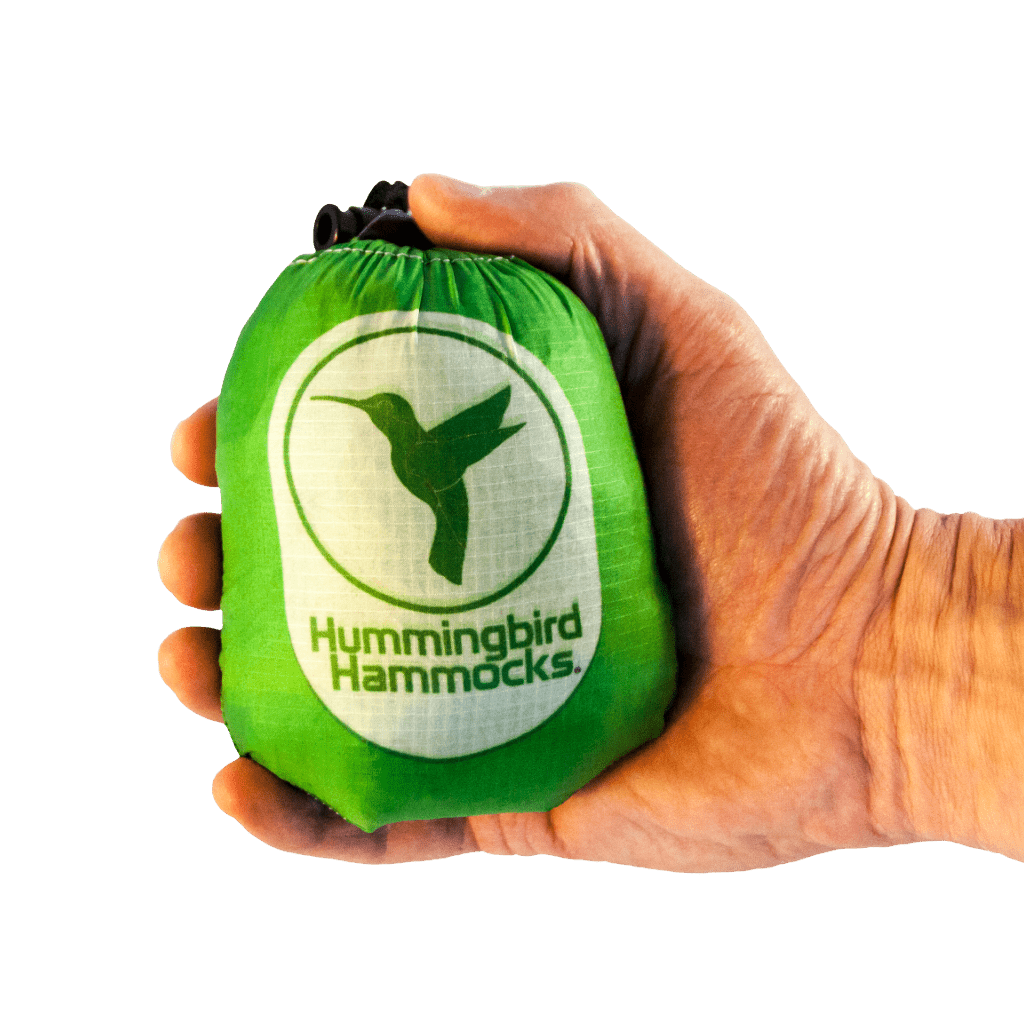 A hand holding a green Hummingbird Hammocks Ultralight Single Hammock bag against a solid green background.