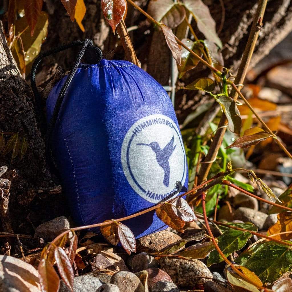 A blue Ultralight Single Hammock from Hummingbird Hammocks placed on rocky ground among dry leaves.