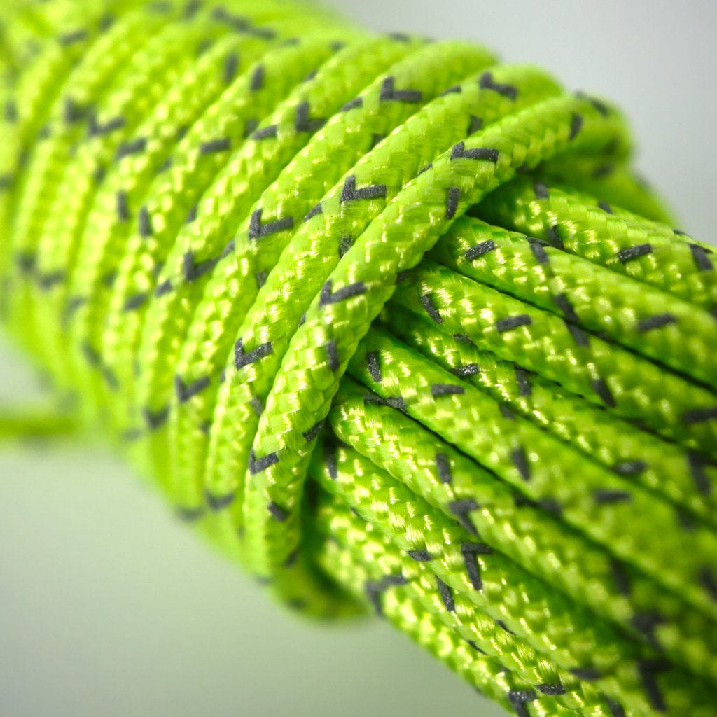 Close-up of a bright green reflective sleeved Hummingbird Hammocks Spectra Guyline Kit with blue speckles, tightly coiled against a light background.