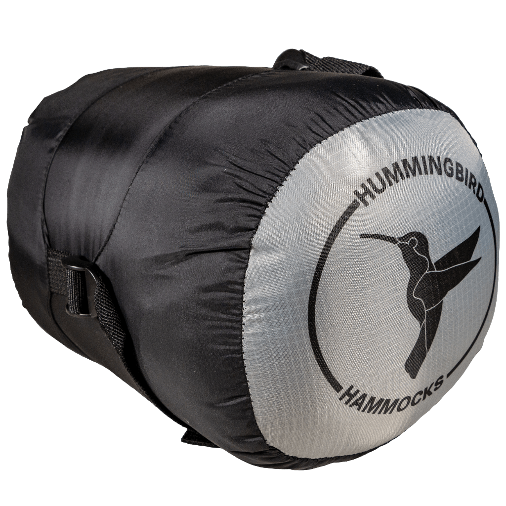 A compact, cylindrical black and gray Puffin Underquilt with the logo "Hummingbird Hammocks" and an image of a hummingbird in flight, featuring a high-quality fill power goose down.